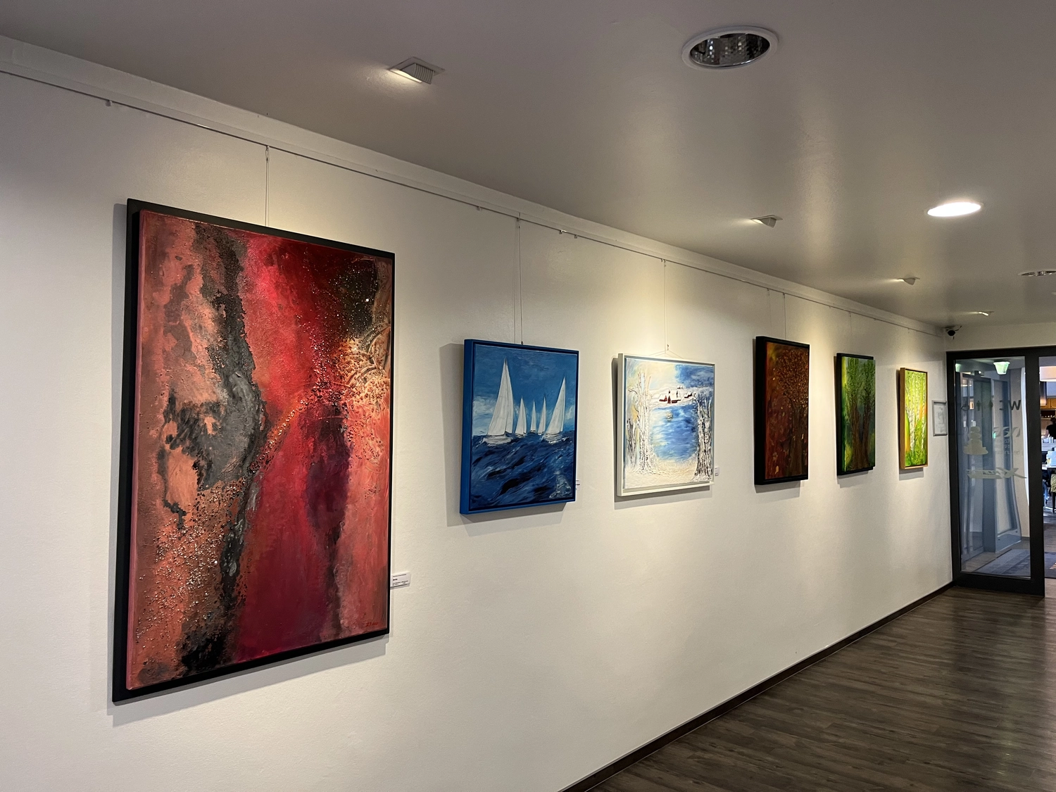 Hannelore Drees-Kiefhaber - Acrylmalerei von der Nordseeküste - Ein hell erleuchteter Flur in einer Kunstgalerie mit sechs gerahmten abstrakten Gemälden an einer weißen Wand und Holzboden.