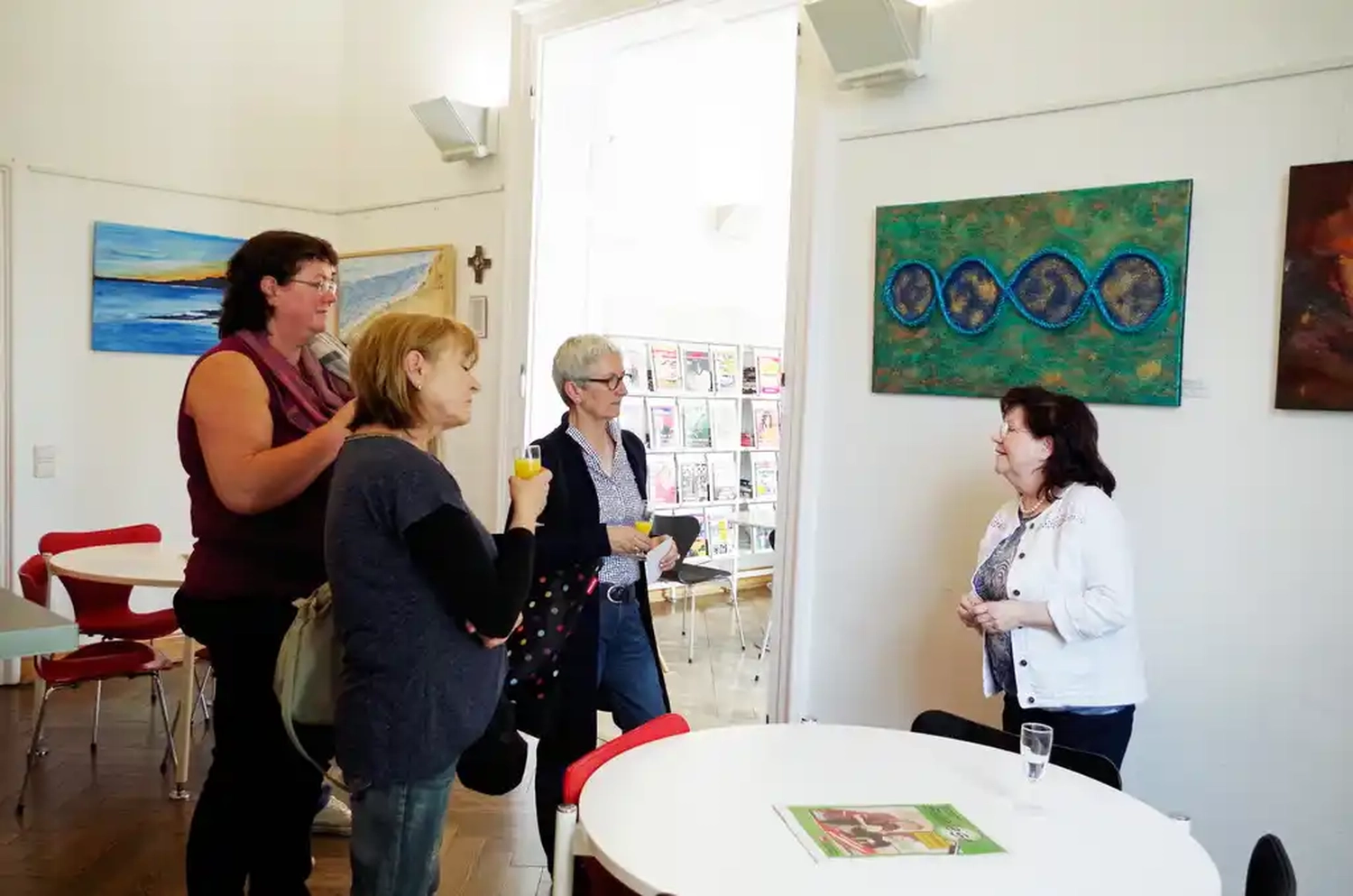 Hannelore Drees-Kiefhaber - Acrylmalerei von der Nordseeküste - Vier Personen unterhalten sich in einer Kunstgalerie oder einem hellen Raum mit einem großen abstrakten Gemälde an der Wand.