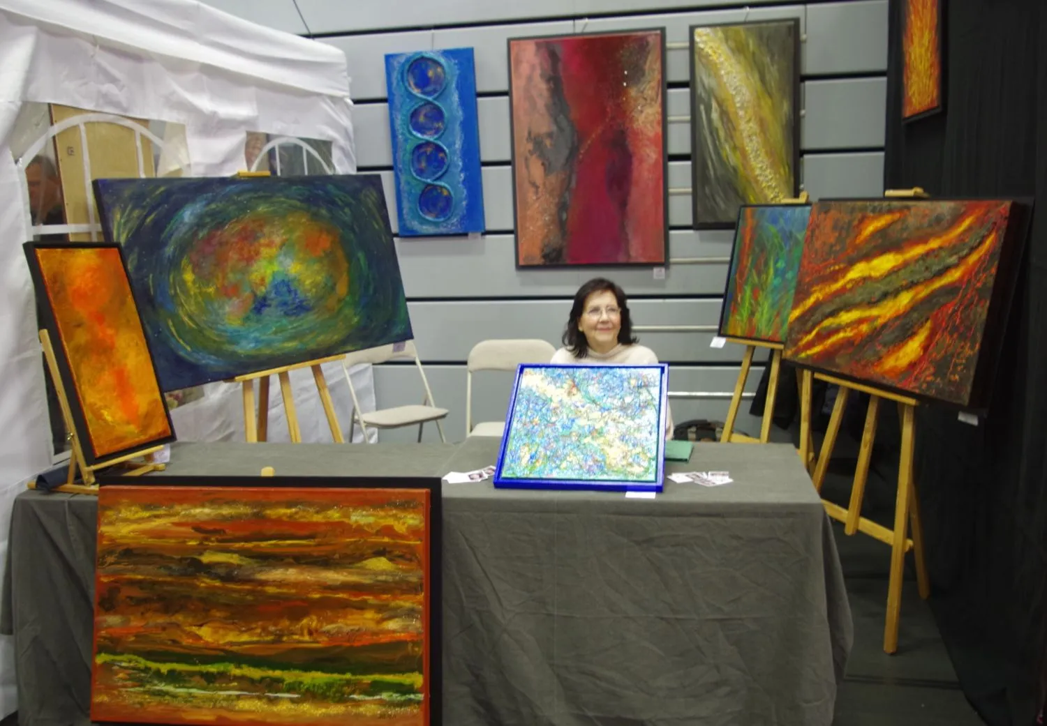 Hannelore Drees-Kiefhaber - Acrylmalerei von der Nordseeküste - Vier Drei Frauen. Die Frau links hält ein blau-gelbes abstraktes Gemälde, die Frau in der Mitte hält ein orange-gelb gerahmtes abstraktes Gemälde und die Frau rechts hält ein rot-oranges abstraktes Gemälde.